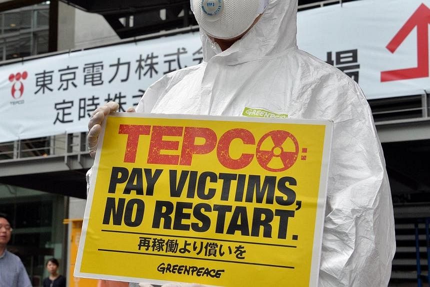 A member of an environmental group Greenpeace wears a radiation protection suit and holds a placard to protest as Tokyo Electric Power Co (TEPCO) holds a shareholders meeting in Tokyo on June 26, 2014.&nbsp;A nuclear plant in southern Japan cleared a