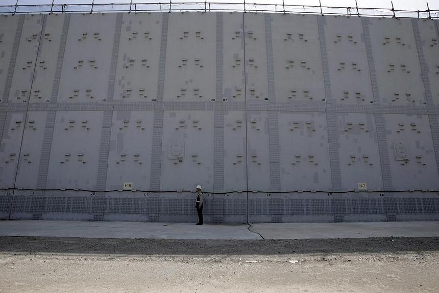 A worker stands in front of an 18-m (59-ft) high and 1.6-km (1-mile) long tsunami defence wall at Chubu Electric Power Co.'s Hamaoka Nuclear Power Station in Omaezaki, Shizuoka Prefecture, in this file picture taken May 17, 2013.&nbsp;Japan's nuclear