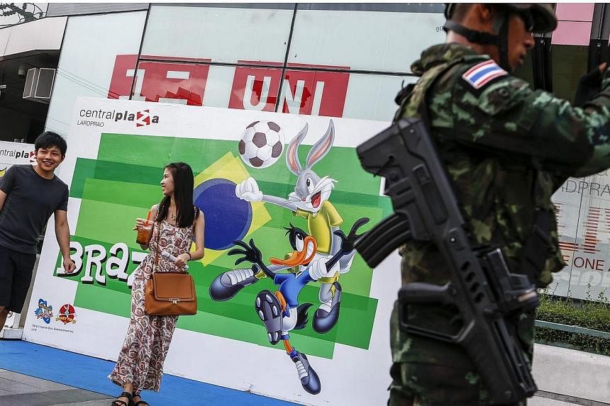A Thai soldier stands next to a billboard to promote the Brazil World Cup 2014 as passers-by walk past outside a shopping mall in Bangkok on June 23, 2014.&nbsp;Police in Thailand said on Tuesday, July 15, 2014, that they had arrested 5,064 people fo