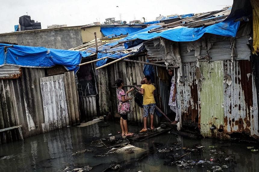 Residents stand in a flooded street outside their house at a slum in Mumbai on July 16, 2014.&nbsp;India's monsoon has covered the entire country, the weather office said on Thursday, July 17, 2014, two days behind the normal schedule in a year that 