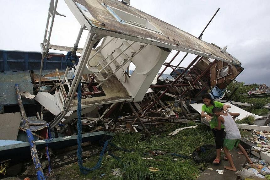 Residents beside a boat destroyed by strong winds brought by Typhoon Rammasun that battered the coastal bay of Baseco compound, metro Manila on July 16, 2014. -- PHOTO: REUTERS