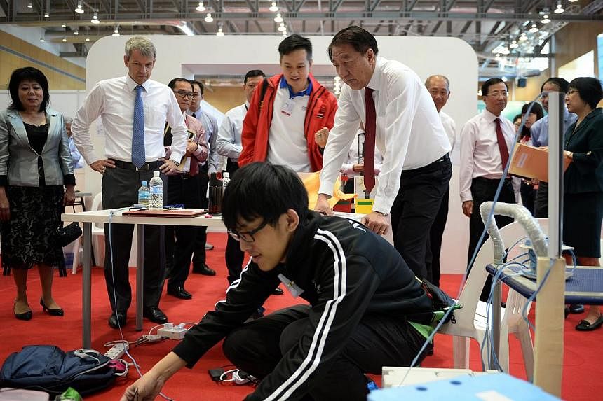 A Nanyang Polytechnic student toggles with his mobile robot as Deputy Prime Minister Teo Chee Hean (far right) and covering chief judge of mobile robotics Clarence Tan observe him, during a tour of the Worldskills Singapore competition held on 10 Jul