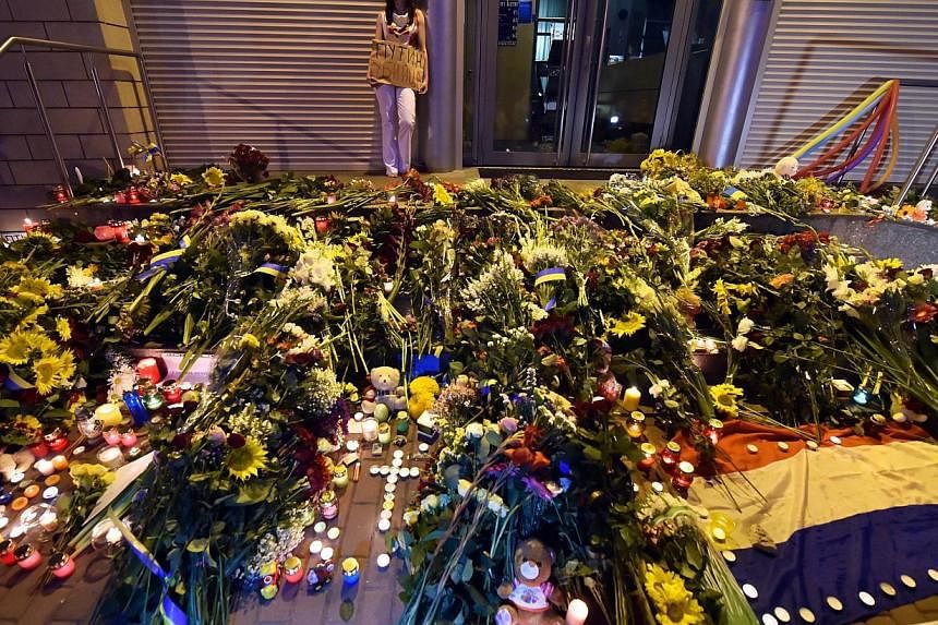 A woman holds a placard reading "Putin is a killer!" near candles and flowers placed in front of the Embassy of the Netherlands in Kiev on July 17, 2014 to commemorate passengers of Malaysian Airlines flight MH17 carrying 298 people from Amsterdam to
