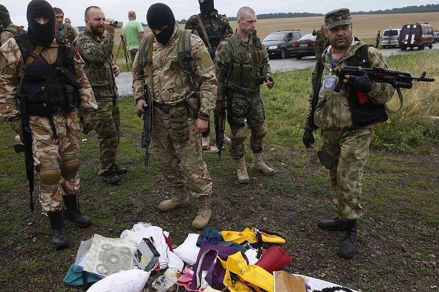 Pro-Russian separatists look at passengers' belongings at the crash site of Malaysia Airlines flight MH17. Looters are reported to have descended on the Ukrainian field where the plane crashed on Thursday and ransacked victims' possessions. -- PHOTO: