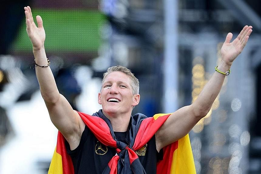 Germany midfielder Bastian Schweinsteiger is draped in the national flag as he celebrates during a victory parade on July 15, 2014, at Berlin's landmark Brandenburg Gate to celebrate their Fifa World Cup title.&nbsp;-- PHOTO: AFP