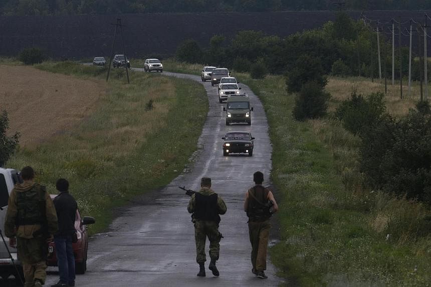 Pro-Russian separatists watch as Organisation for Security and Cooperation in Europe (OSCE) monitors arrive at the crash site of Malaysia Airlines flight MH17, near the settlement of Grabovo in the Donetsk region on July 18, 2014.&nbsp;Malaysian Tran