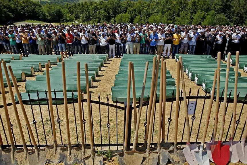 Bosnian Muslims pray in front of coffins of their relatives during a mass funeral in the village of Biscani, near Prijedor, on Sunday, July 20, 2014. The remains of 284 victims of the Bosnian war were laid to rest on Sunday having been unearthed from