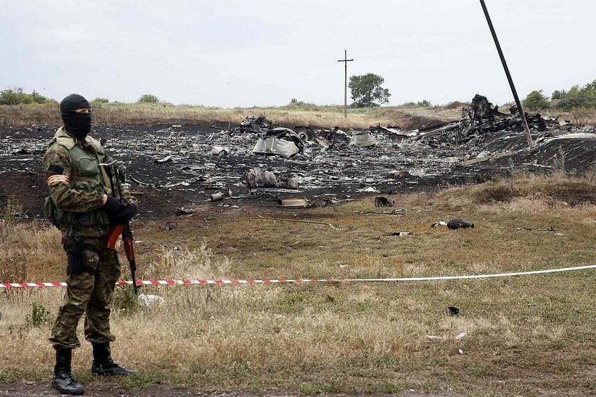 A pro-Russian separatist stands near a body at the crash site of Malaysia Airlines Flight MH17, near the settlement of Grabovo in the Donetsk region on July 19, 2014. -- PHOTO: REUTERS