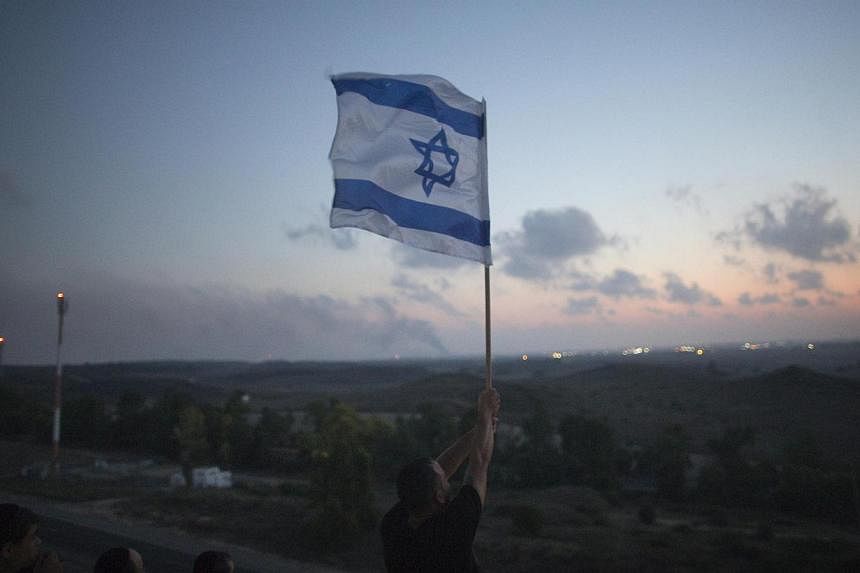 An Israeli man holds up a flag atop a hill overlooking the Gaza Strip in the southern town of Sderot on July 20, 2014. -- PHOTO: REUTERS