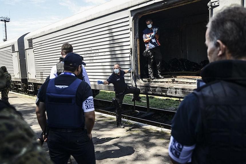 Monitors from the Organisation for Security and Cooperation in Europe (OSCE) and members of a forensic team inspect a refrigerator wagon containing the remains of victims from the downed Malaysia Airlines Flight MH17 at a railway station in the easte