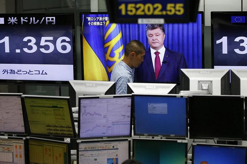 An employee of a foreign exchange trading company in Tokyo walks past a monitor showing Ukrainian President Petro Poroshenko. Asian markets picked up on Tuesday with traders welcoming news that pro-Russian rebels had handed over the black boxes from 