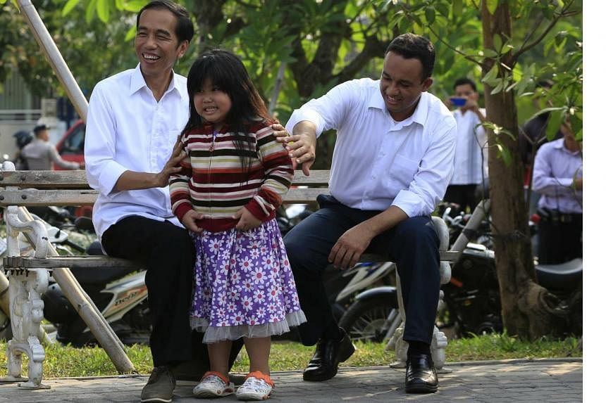 Indonesian presidential candidate Joko "Jokowi" Widodo (L) poses with a child beside his colleague Anies Baswedan while waiting for the announcement of poll results by the Elections Commission, at Waduk Pluit in Jakarta July 22, 2014 -- PHOTO: AFP