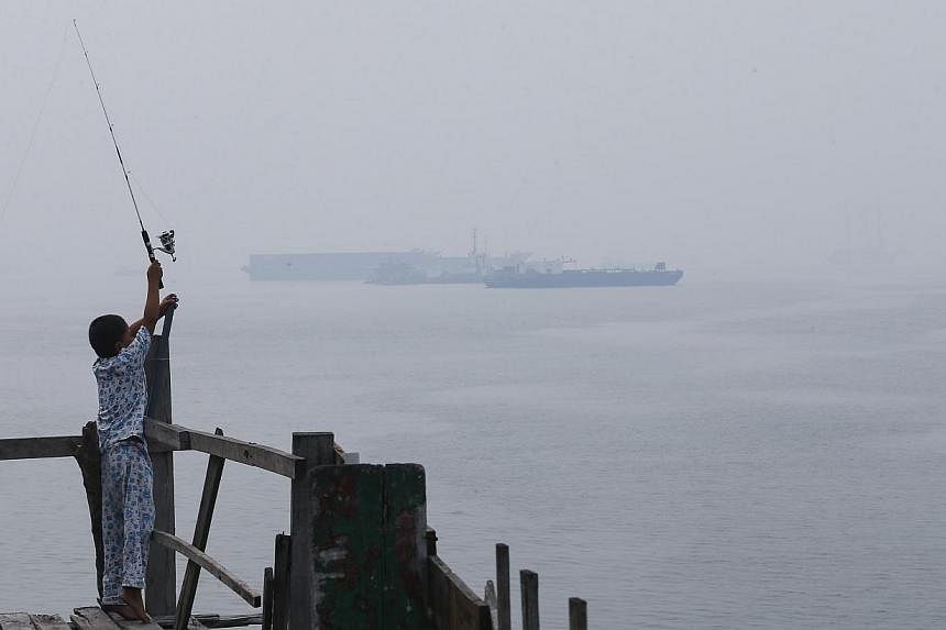 A boy fishes at a jetty, as a ship is seen in the background through haze, at Northport Klang, outside Kuala Lumpur on June 24, 2014.&nbsp;The Air Pollutant Index (API) of Perak's coastal town Seri Manjung has nearly doubled since last night, hitting