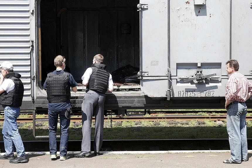 Monitors (left) from the Organization for Security and Cooperation in Europe inspect a refrigerator wagon, which according to employees and local residents contains bodies of passengers of the crashed Malaysia Airlines Boeing 777 plane, at a railway 