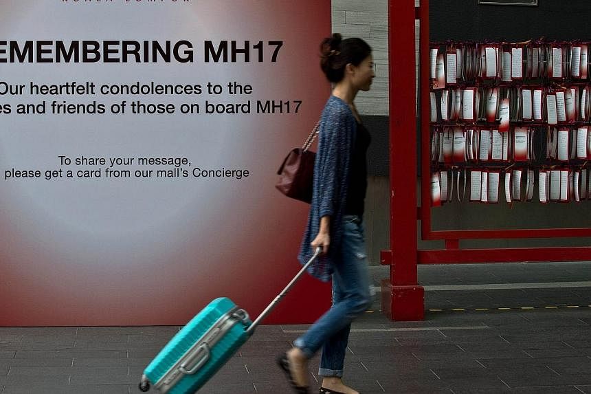 A tourist walks past a board with prayers and condolence messages for victims of the Malaysia Airlines MH17 flight, displayed on a board outside a shopping mall in Kuala Lumpur on July 23, 2014. -- PHOTO: AFP