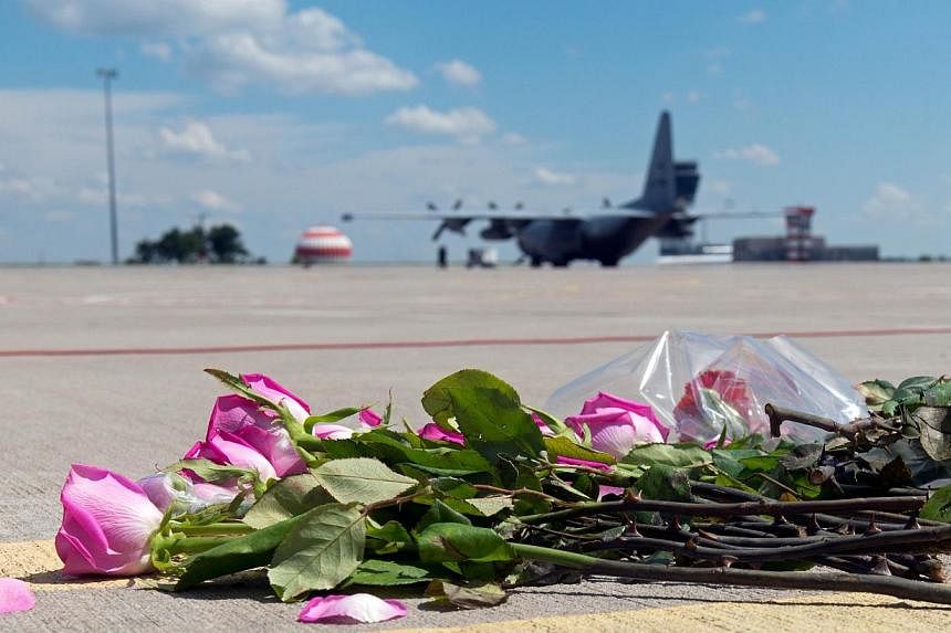 Flowers lay on the tarmac as a ground Hercules transport aircraft of the Royal Dutch Airforce, carrying bodies from downed Malaysia Airlines Flight MH17, prepares to take off from Kharkiv airport on July 23, 2014.&nbsp;Two aircraft carrying the remai