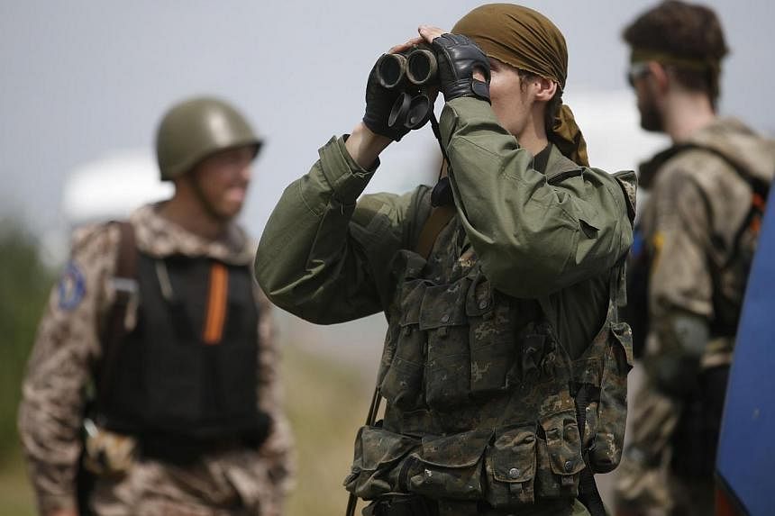 An armed pro-Russian separatist uses a pair of binoculars as he stands guard while monitors from the Organisation for Security and Cooperation in Europe (OSCE) and a team of Malaysian air crash investigators inspect the crash site of Malaysia Airline