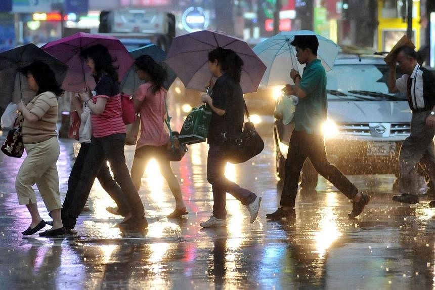 Pedestrians shield themselves from the rain with umbrellas as they cross a street in Taipei on July 22, 2014 as Typhoon Matmo approaches eastern Taiwan. -- PHOTO: AFP