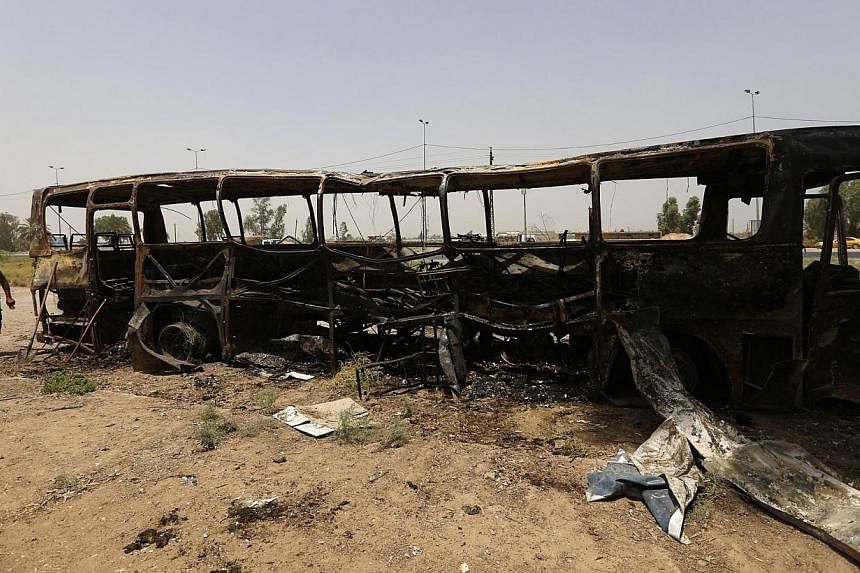 &nbsp;A man walks past a burnt bus in Taji, north of Baghdad on Thursday, July 24, 2014.&nbsp;An onslaught on a convoy transferring inmates north of Baghdad left dozens dead on Thursday, as visiting UN chief Ban Ki Moon said Iraq's survival hinged on