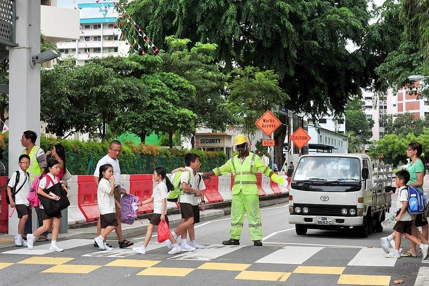 A traffic marshal directing a lorry along the special access road off the Central Expressway. A traffic marshal guiding pupils from Hong Wen School across a zebra crossing. Singapore Power has taken various safety measures, including deploying traffi