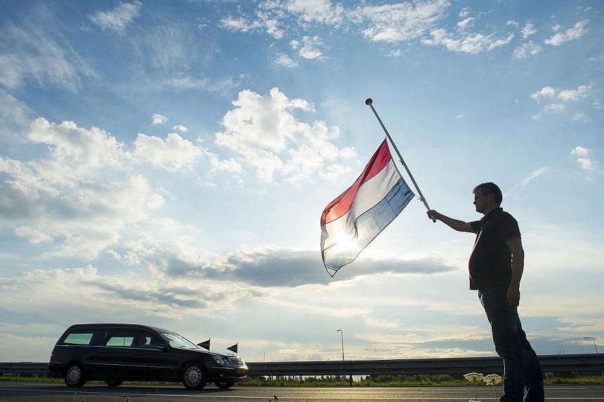 Dutch Ronald Visee holds a Netherlands flag flying at half-mast (right) as a hearse carrying the remains of victims of the Malaysia Airlines flight MH17 plane disaster are escorted on highway A27 near Nieuwegein by military police, on their way to be