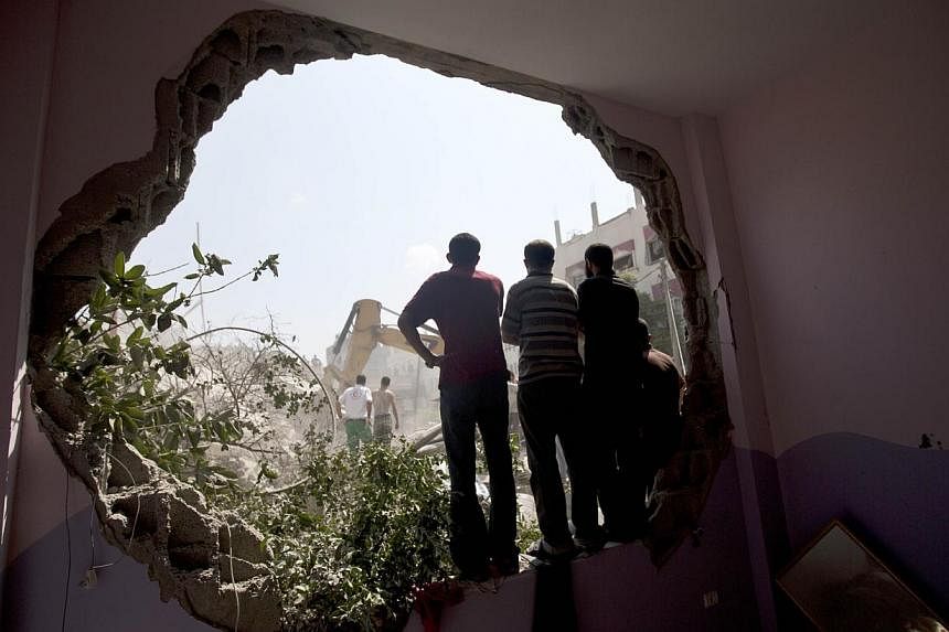 Palestinians stand watching from a whole in a wall as Civil Defence workers remove the rubble of a building destroyed in an Israeli air strike, in Gaza City, on July 21, 2014.&nbsp;The UN Security Council on Monday called for an immediate humanitaria
