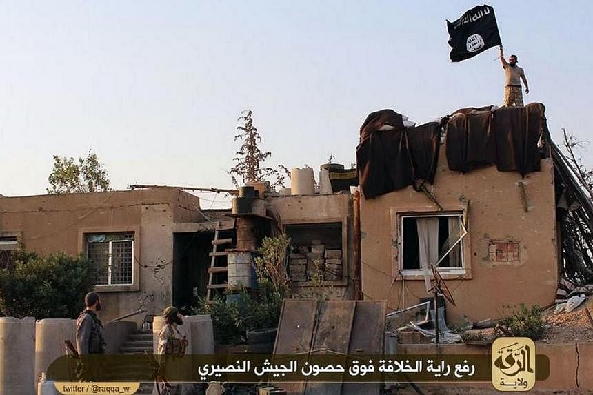 An image made available by Jihadist media outlet Welayat Raqa on July 25, 2014, shows allegedly shows members of the IS (Islamic state) militant group raising their black and white flag over a building belonging to a Syrian army base in the northern 