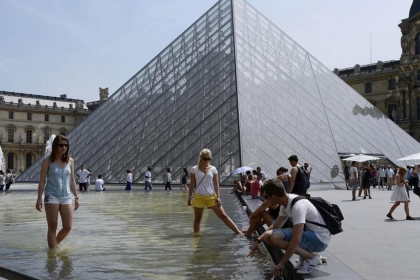 People take in the sun near a fountain in front of the Louvre Pyramid in Paris on July 18, 2014. -- PHOTO: AFP