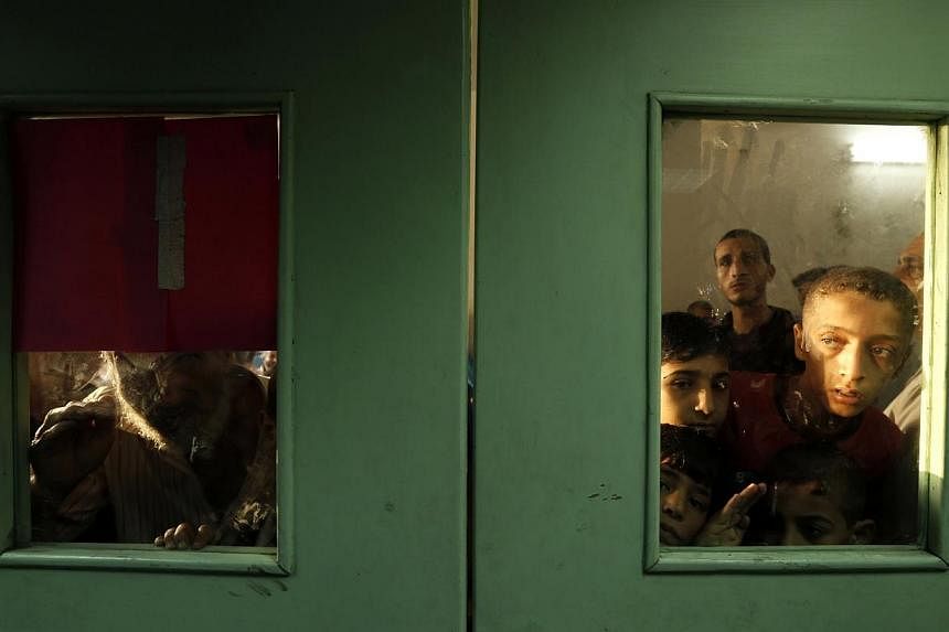 Palestinians look out from behind the doors at Kamal Edwan hospital where victims have been brought following an Israeli strike on a compound housing a UN school in Jabalia refugee camp in the northern Gaza Strip early on July 30, 2014. -- PHOTO: AFP