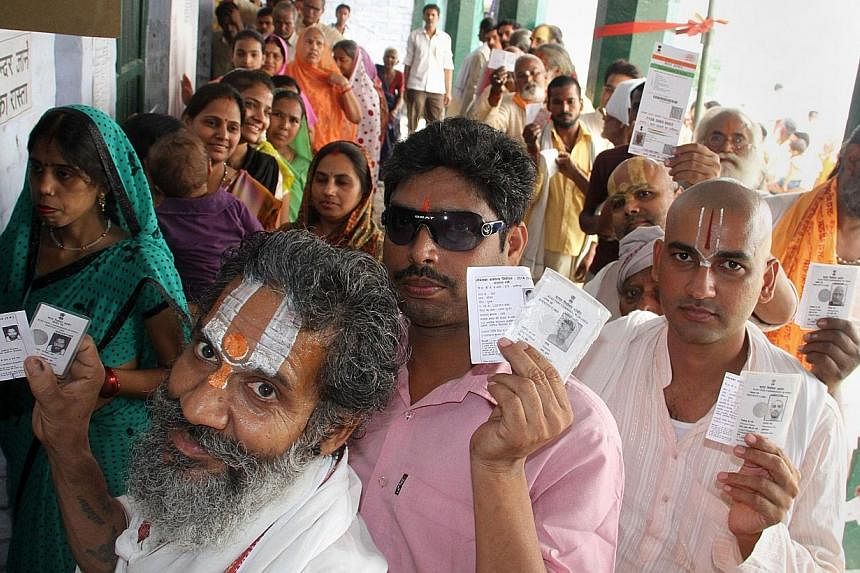 Indian voters display their identification cards as they wait to cast their ballots at a polling station in Ayodhya on May 7, 2014. Instead of throwing out the unique identification card Aadhaar, created by the previous government, the Modi regime wi