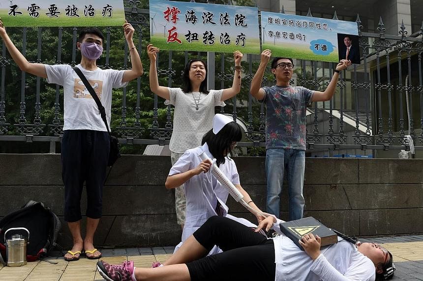 Xiao Tie, executive director of the Beijing LGBT Centre, pretends to inject a patient with a mock syringe during a protest outside the Haidian District Court in Beijing on Thursday, July 31, 2014, as the court began hearing a landmark case on "gay co