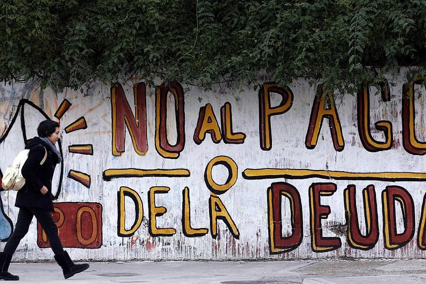 A woman walks past a graffiti that reads "No to the debt payment" in Buenos Aires on July 28, 2014.&nbsp;Ratings agency Fitch declared Argentina in default on its bonds for the second time in 13 years on Thursday after talks between Buenos Aires and 