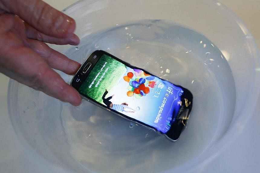 P2i's CEO Carl Francis demonstrates a mobile phone, treated with their thin, transparent, splash-resistant polymer coat, functioning in water, during an interview with Reuters in Singapore, on July 31, 2014. -- PHOTO: REUTERS