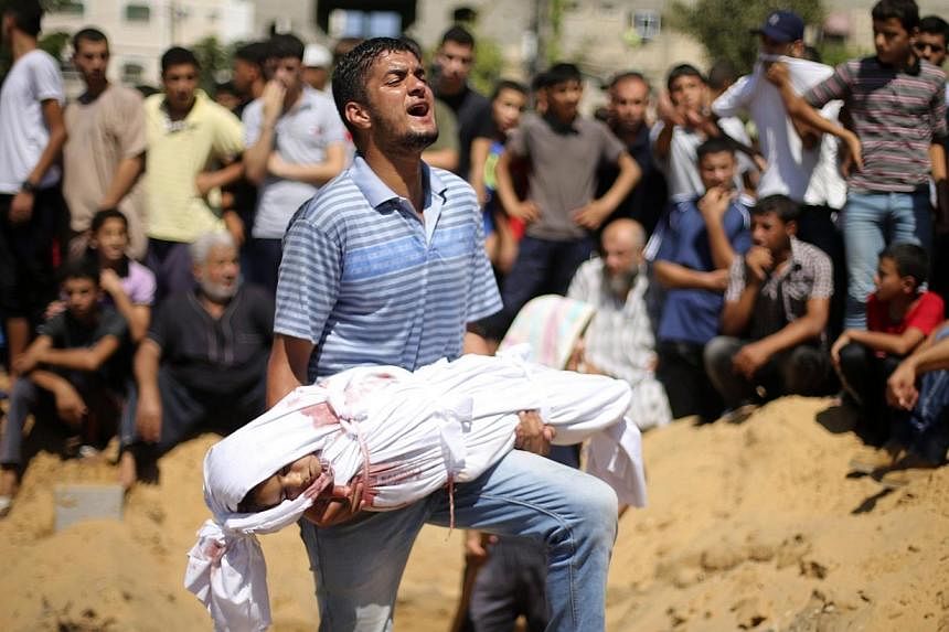 A Palestinian man reacts as he carries the body of a girl from the Abu Nejim family, whom medics said was killed along with other eight family members by an Israeli air strike, before her burial at a cemetery in Beit Lahiya in the northern Gaza Strip