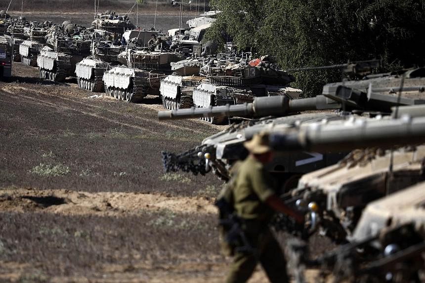 An Israeli soldier walks past Merkava tanks positioned on the Israeli side of the border with the Palestinian enclave as the sun sets on Aug 3, 2014.&nbsp;Palestinian groups, including representatives from Hamas and Islamic Jihad, held their first fo