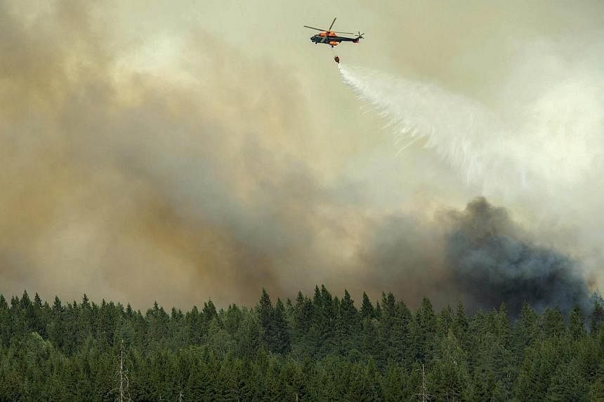 A helicopter drops its load of water on the wildfire front just outside the evacuated village of Gammelby near Sala, central Sweden, on Aug 4, 2014.&nbsp;-- PHOTO: AFP