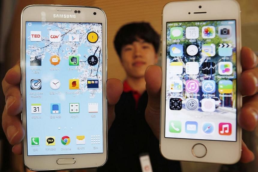 A sales assistant holding Samsung Electronics' Galaxy 5 smartphone (left) and Apple Inc's iPhone 5 smartphone poses for photographs at a store in Seoul on July 16, 2014. -- PHOTO: REUTERS