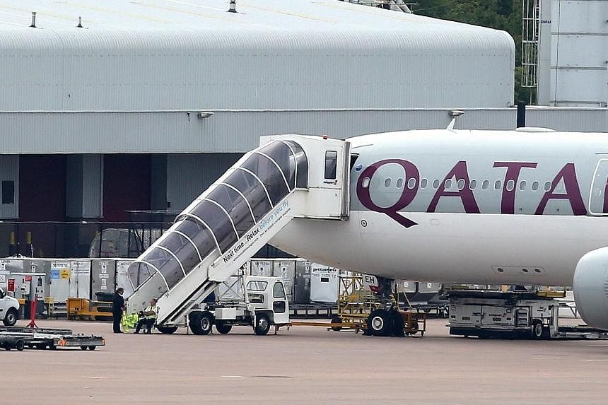 Airport personnel are seen at the foot of the stairs of the Qatar Airways plane that was forced to make an emergency landing at Manchester Airport on Aug 5, 2014. -- PHOTO: AFP