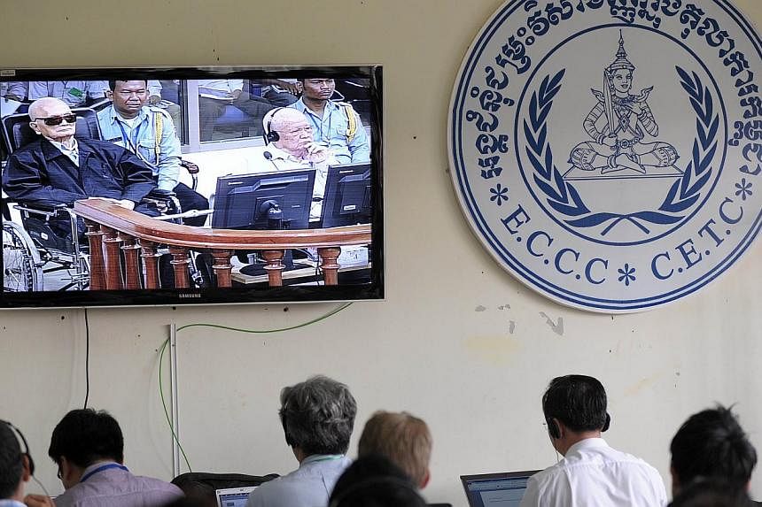 Cambodian and international journalists watch a live video feed showing former Khmer Rouge leader "Brother Number Two" Nuon Chea (left) and former Khmer Rouge head of state Khieu Samphan (right) in the courtroom during their trial at the Extraordinar