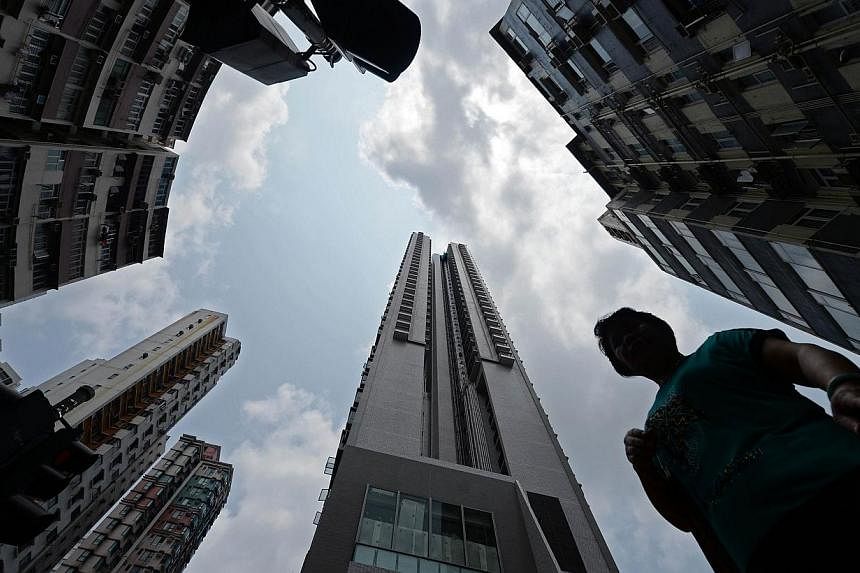 In this picture taken on August 2, 2014, a woman waits at a pedestrian crossing surrounded by residential buildings in Hong Kong.&nbsp;At a glitzy show stall for a new residential development in Hong Kong, property agents with loudspeakers are promot