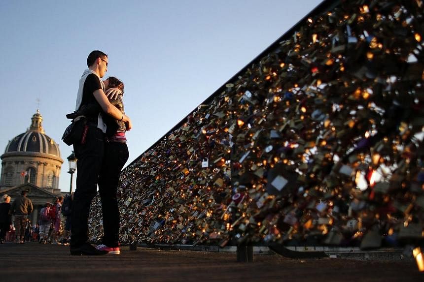 A couple embraces during sunset on the Pont des Arts with its fence covered with padlocks clipped by lovers over the River Seine in Paris, in this August 10, 2013 file photo. -- PHOTO: REUTERS