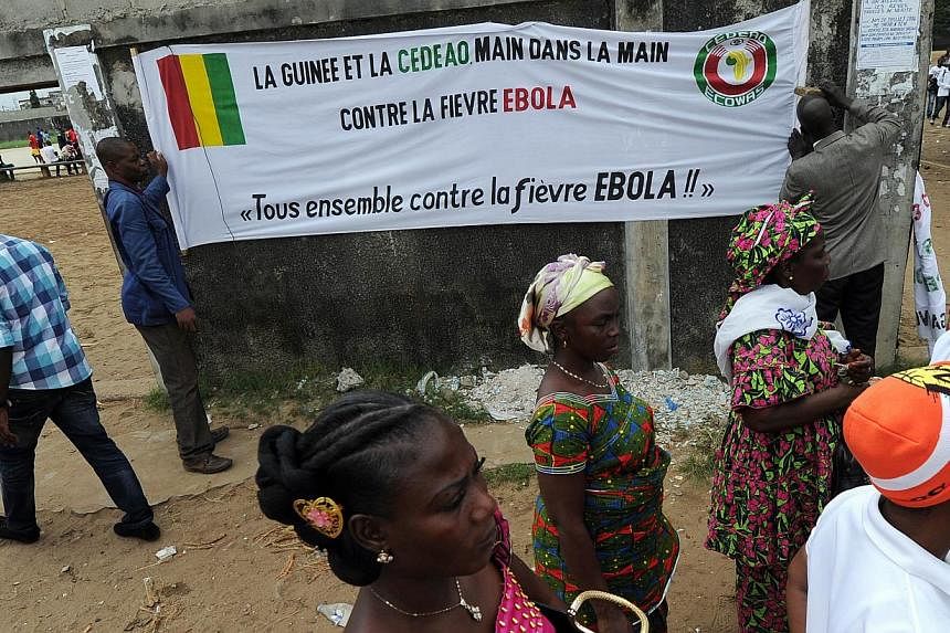 People walk in front of a banner reading ''Guinea and ECOWAS hands in hands against Ebola fever ''All together against Ebola fever!'' '' prior to a youth football tournament near the Koumassi sports center in Abidjan on Aug 10, 2014. &nbsp;-- PHOTO: 