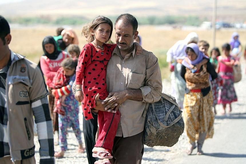 A displaced Iraqi man from the Yazidi community carries his daughter as they cross the Iraqi-Syrian border at the Fishkhabur crossing, in northern Iraq, on Aug 11, 2014. -- PHOTO: AFP