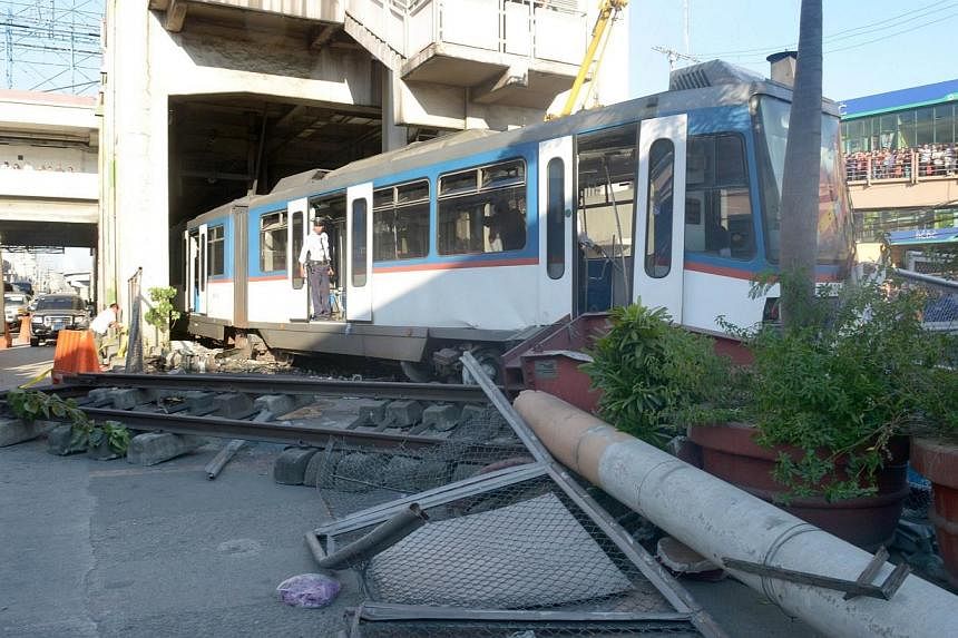 Rescue workers investigate at the scene after an overhead commuter train (centre) overshot the last station, causing it to derail and smash through a wall in Manila on Aug 13, 2014.&nbsp;-- PHOTO: AFP
