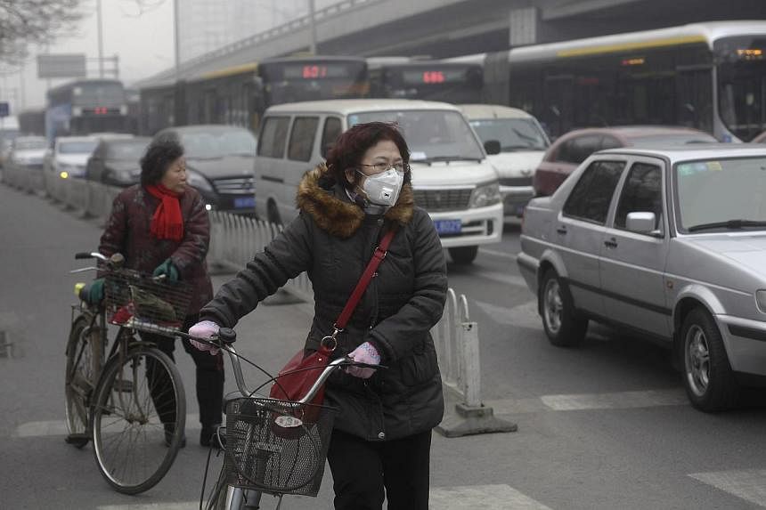 A woman wearing a mask stands beside her bicycle at a traffic junction in Beijing amid thick haze on Feb 25, 2014. -- PHOTO: REUTERS