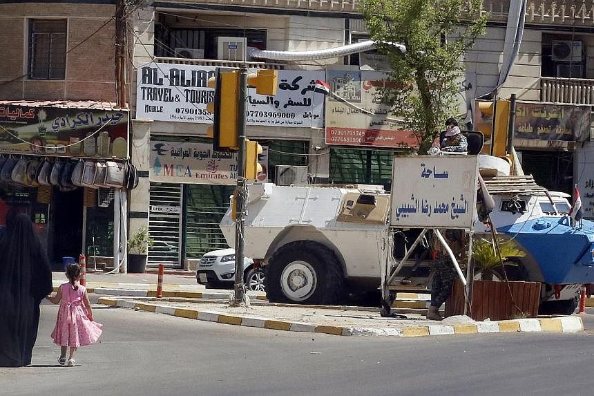 An Iraqi woman and child walk towards an Iraqi security armoured personnel carrier stationed along a street as daily life in neighbourhoods and the commercial centre function normally in the capital Baghdad, on August 12, 2014. A political showdown l