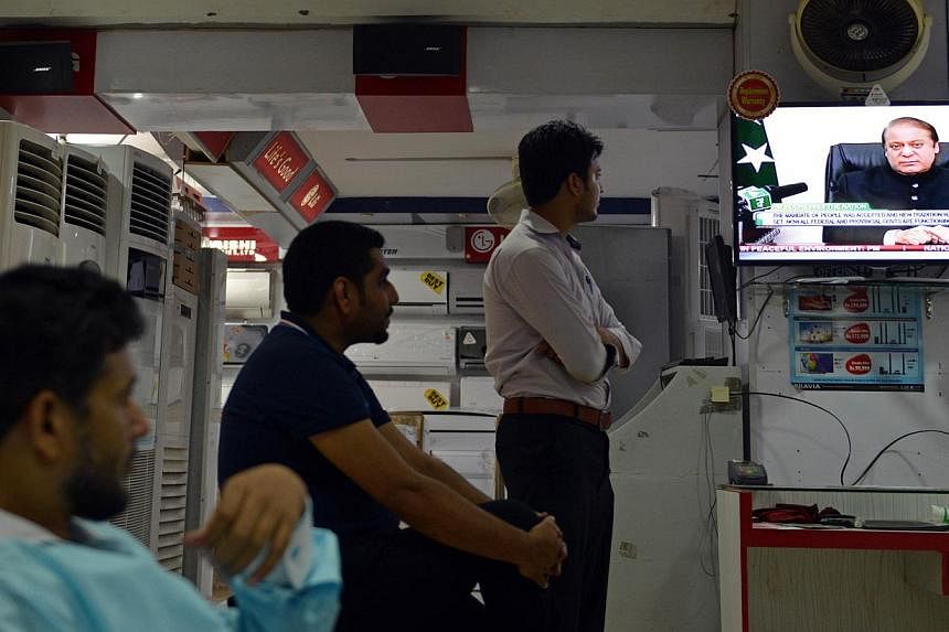 People listen to a broadcast speech by Pakistani Prime Minister Nawaz Sharif on a television in an electronics market in Islamabad on August 12, 2014. In a televised address to the nation, Mr Sharif said he was requesting the Supreme Court to form a 