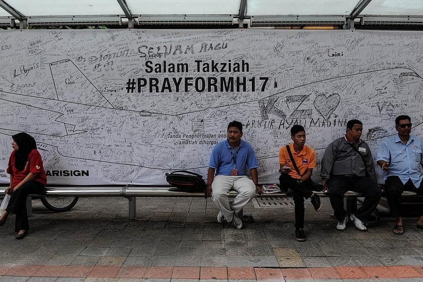 People sit in front a banner showing prayers and well-wishes for passengers onboard Malaysia Airlines flight MH17 that crashed in eastern Ukraine, at a bus stop in Kuala Lumpur on Aug 4, 2014. -- PHOTO: AFP