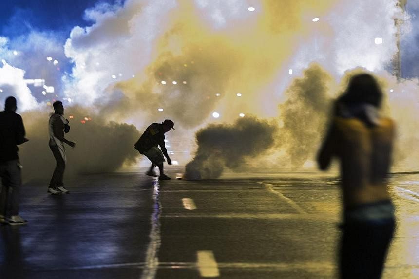 A protester reaches down to throw back a smoke canister as police clear a street after the passing of a midnight curfew meant to stem ongoing demonstrations in reaction to the shooting of Michael Brown in Ferguson, Missouri on Sunday, Aug 17, 2014.&n