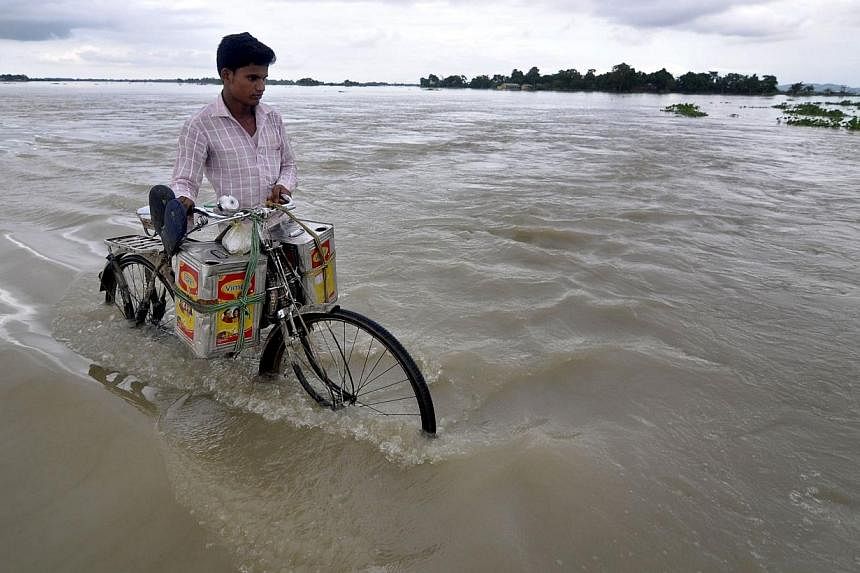 An Indian villager pushes his bicycle along a submerged road in the flood affected village of Ashigarh, some 70km from Guwahati on Aug 16, 2014.&nbsp;Floods triggered by heavy rains have inundated nearly 1,500 villages in northern India, killing at l